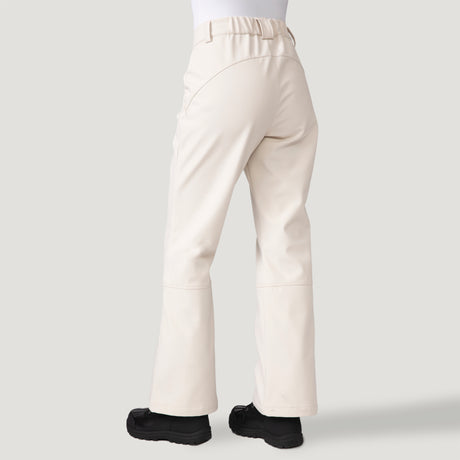 A person wears Free Country Women's Stormlite Super Softshell® Ski Pant in off-white, featuring water resistance, elastic waistband, and a relaxed straight-leg fit. Shown from the back against a plain light gray background with black shoes.