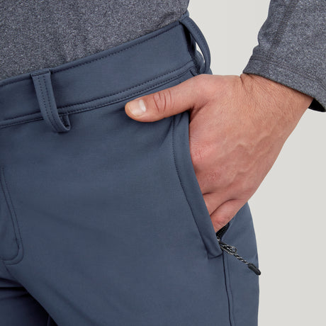 A person wearing Clearance Men's Ascend Flex Softshell Ski Pants in gray and a matching long-sleeve shirt places their right hand in the front pocket, revealing a small zipper pull near the pocket opening.