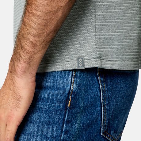 [Jacob is 6’1.5" wearing size M] Close-up of a person wearing a gray t-shirt with a brand logo and blue jeans on a white background.