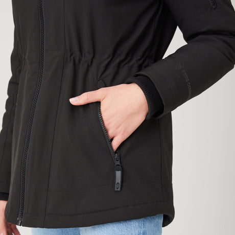 Woman wearing Free Country Women's Thermo Super Softshell® Long Jacket in black with a full front zipper opening, lower pockets, diamond quilted lining, a hood with an adjustable drawcord, and water resistant and wind resistant stretch performance fabric, light grey background. Best women’s jacket for winter weather.