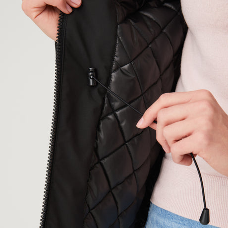 Woman wearing Free Country Women's Thermo Super Softshell® Long Jacket in black with a full front zipper opening, lower pockets, diamond quilted lining, a hood with an adjustable drawcord, and water resistant and wind resistant stretch performance fabric, light grey background. Best women’s jacket for winter weather.
