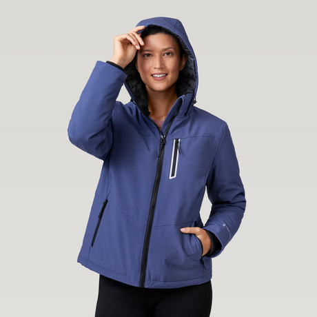 A woman wearing the Clearance Women's Thermo Super Softshell® Ski Jacket in blue smiles at the camera, holding the hood. The jacket features zippered pockets and a white vertical chest zipper against a plain light gray background.