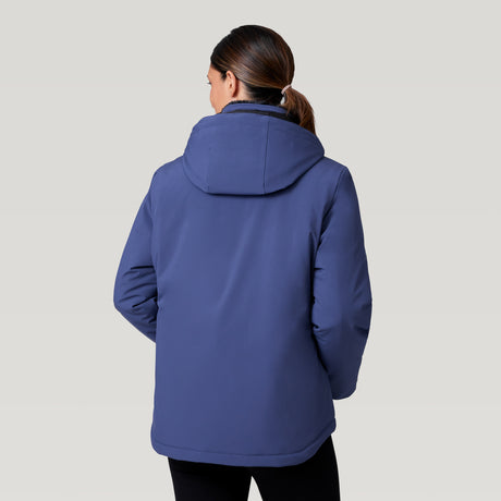 A woman with brown hair in a ponytail is seen from behind wearing the Women's Thermo Super Softshell® Ski Jacket by Clearance and black pants, standing against a plain light gray background.