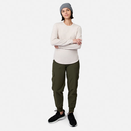 A person wearing a grey beanie, long-sleeved cream shirt, olive green Women’s Get Out There Fleece Lined Jogger, and black sneakers stands with arms crossed.