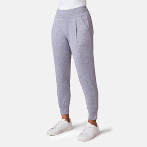 A person wears the Free Country Women's Cloud Knit Pleated Jogger in light gray, featuring a high waistband and pleated front with four-way stretch, styled with a white top and sneakers against a plain white background.