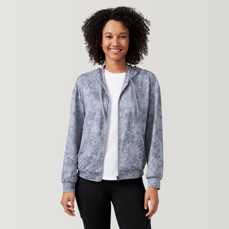 A woman with curly hair smiles while wearing a light gray Clearance Women's Cloud Knit Zip Hoodie over a white shirt and black pants, standing against a plain, light background.