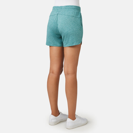 A woman models the Free Country Women's Cloud Knit Shorts in teal with four-way stretch, paired with white sneakers, shown from the back against a plain white background.