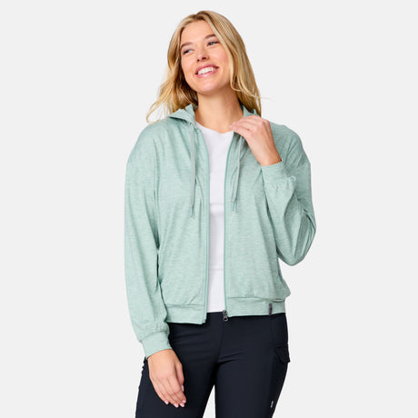 A smiling woman with long blonde hair wears a Clearance Women's Cloud Knit Zip Hoodie in light green over a white shirt and black pants, standing against a plain light gray background.