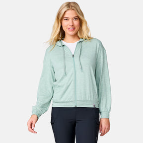A woman in a Women's Cloud Knit Zip Hoodie by Clearance, light green in color, over a white top and black pants smiles against a plain light background.