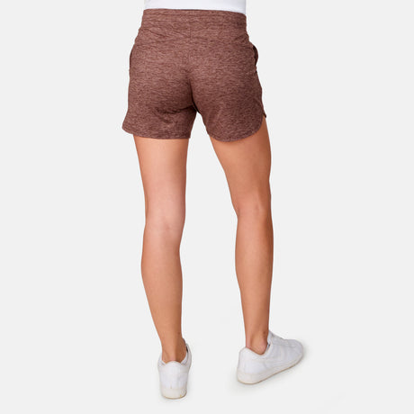 A person stands with their back to the camera against a plain white background, wearing maroon heathered Women's Cloud Knit Shorts by Free Country featuring four-way stretch, paired with white sneakers.