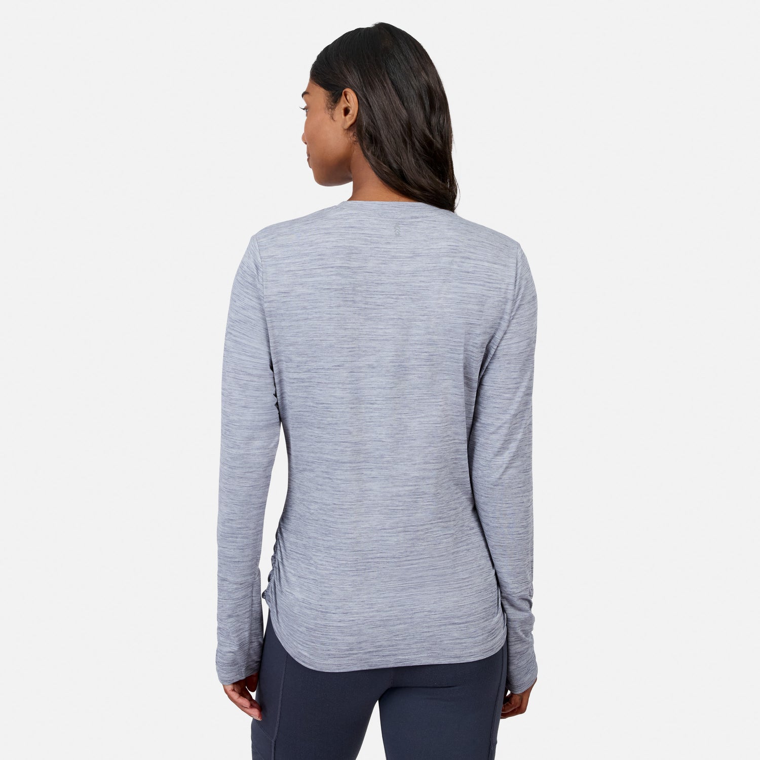 A woman with long dark hair, seen from behind, wears the Free Country Women’s Cloud Knit Crew Neck Top in light gray and dark pants against a plain white background.