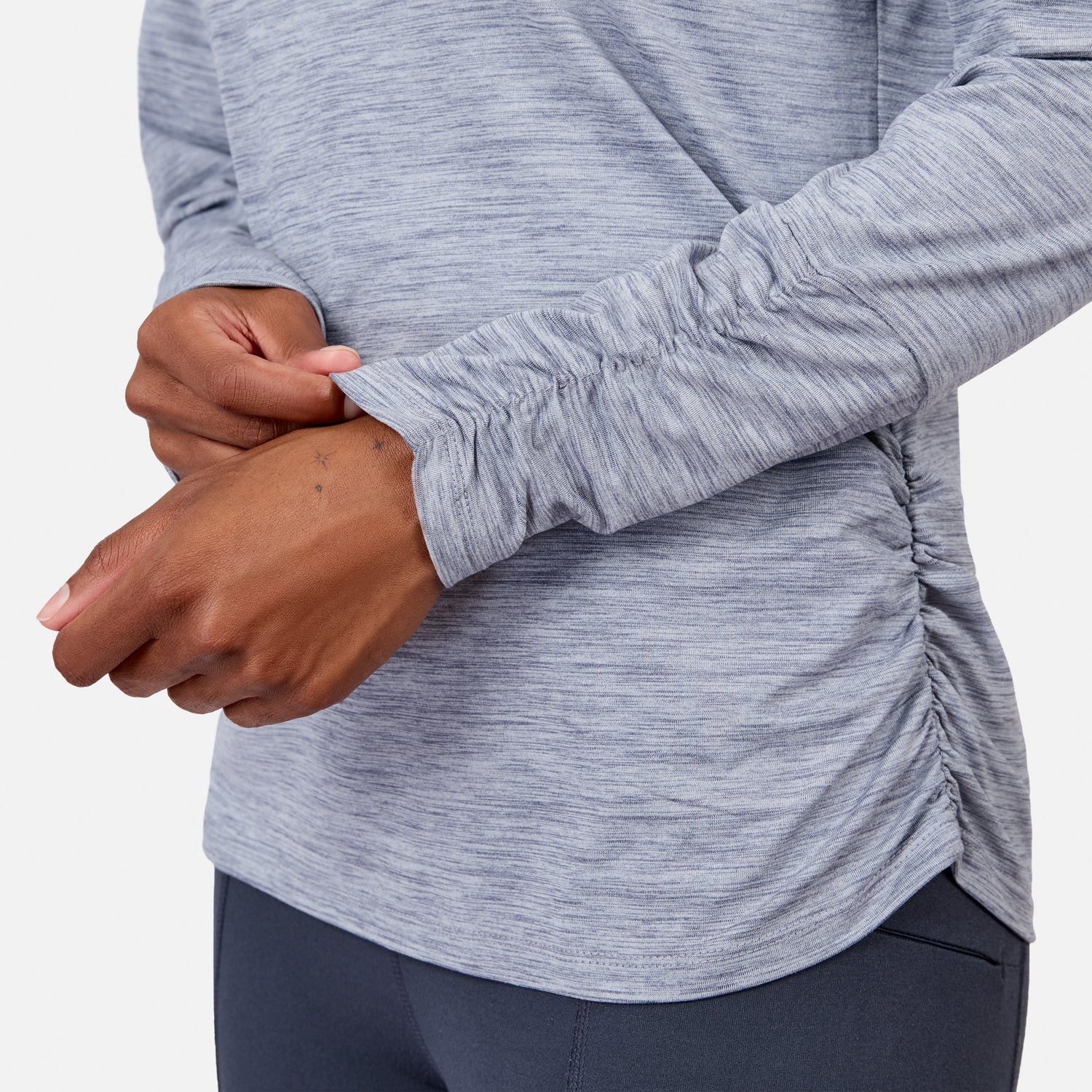 A person adjusts the ruched sleeve of the Women’s Cloud Knit Crew Neck Top by Free Country, shown in light gray with moisture-wicking fabric against a plain white background.