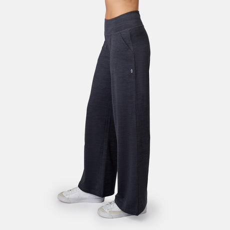 A person in dark gray Free Country Women’s Cloud Knit Wide Leg Pants and white sneakers, shown from the waist down against a plain white background.