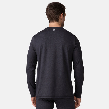 A man with short brown hair is seen from behind, wearing a dark charcoal Men's Cloud Knit Base Layer Top by Clearance. The moisture-wicking shirt has a small logo on the upper back. He pairs it with matching pants against a plain white background.
