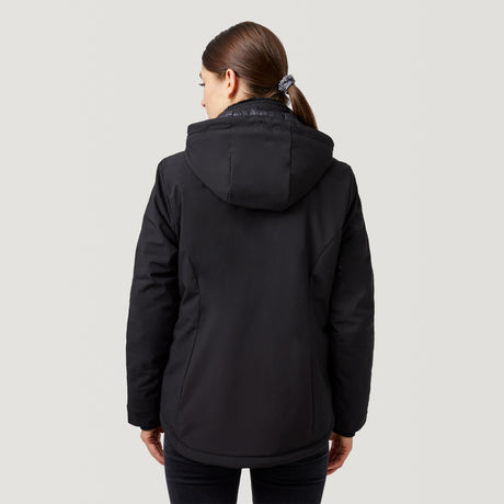 A woman with brown hair in a ponytail stands with her back to the camera, wearing the Clearance Women's Thermo Super Softshell® Ski Jacket and black pants against a plain light gray background.