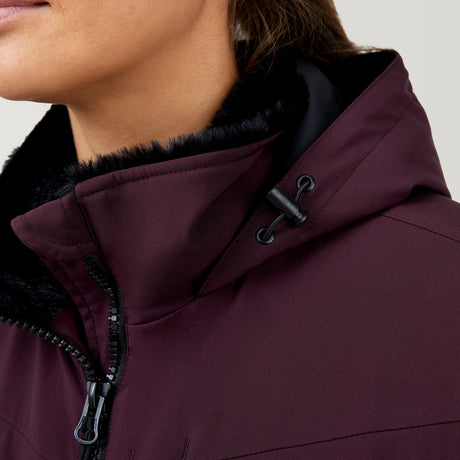 Close-up of a person wearing the Clearance Women's Thermo Super Softshell® Ski Jacket in maroon, featuring water resistance, black faux fur lining, and a drawstring hood. The jacket is zipped up, partially revealing the person's face and neck.