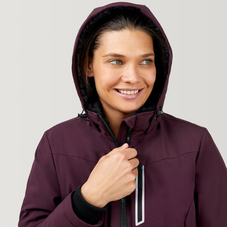 A person smiles while wearing the Clearance Women's Thermo Super Softshell® Ski Jacket in maroon, featuring a zipper and chest pocket, holding the collar closed. The background is plain light gray.