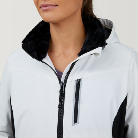 Close-up of a person wearing the Women's Thermo Super Softshell® Ski Jacket by Clearance. The white, water-resistant jacket has black faux fur collar, black zipper, zippered chest pocket, side panels, and a partially visible hood. Face is partially shown.