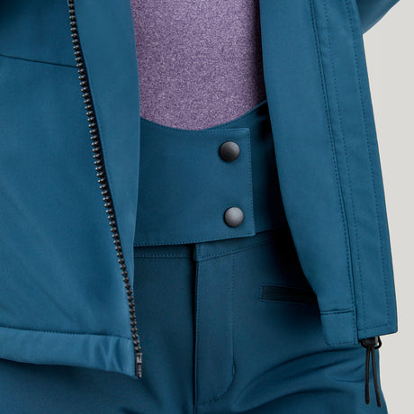 A close-up shows a person in teal pants with two black buttons, a light purple top, and a partially unzipped Clearance Women's Thermo Super Softshell® Ski Jacket, revealing the waistband and part of the top.