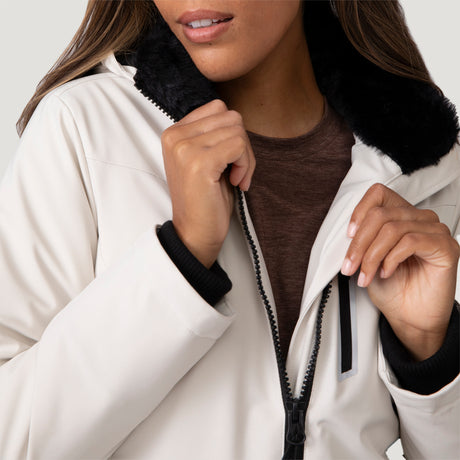 A woman, partially visible, zips up the Clearance Women's Thermo Super Softshell® Ski Jacket—light-colored with a black fleece collar—over a brown shirt, her hands on the water-resistant coat’s zipper and collar.