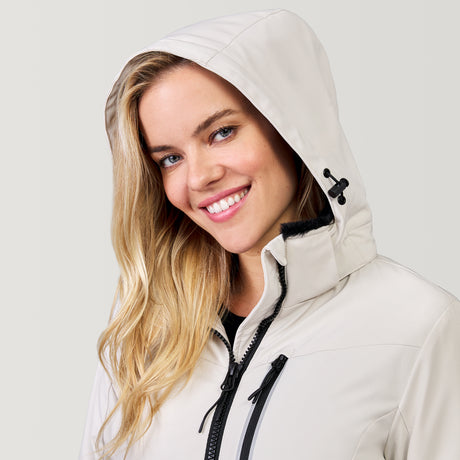 [Model is wearing a size Small.] Woman wearing Free Country Women's FreeCycle® Thermo Super Softshell® II Jacket in white with a full front zipper opening, lower pockets, soft lining, a detachable hood with an adjustable drawcord, and water resistant and wind resistant stretch performance fabric, light grey background. Best women’s jacket for winter weather.