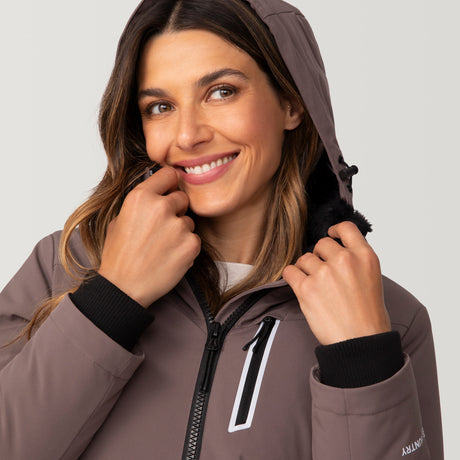 [Olga is 5’9" wearing a size Small.] Woman wearing Free Country Women's FreeCycle® Thermo Super Softshell® II Jacket in light brown with a full front zipper opening, lower pockets, soft lining, a detachable hood with an adjustable drawcord, and water resistant and wind resistant stretch performance fabric, light grey background. Best women’s jacket for winter weather.