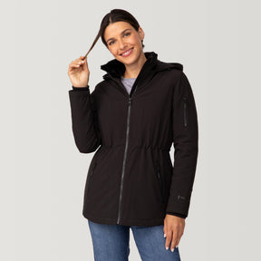 [Olga is 5’9" wearing a size Small.] Woman wearing Free Country Women's Thermo Super Softshell® Long Jacket in black with a full front zipper opening, lower pockets, diamond quilted lining, a hood with an adjustable drawcord, and water resistant and wind resistant stretch performance fabric, light grey background. Best women’s jacket for winter weather.