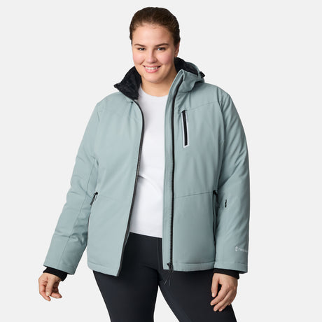 A woman wears the Free Country Women's Plus Size FreeCycle® Thermo Super Softshell® II light blue jacket with black zippers over a white shirt and black pants, smiling against a plain light background.