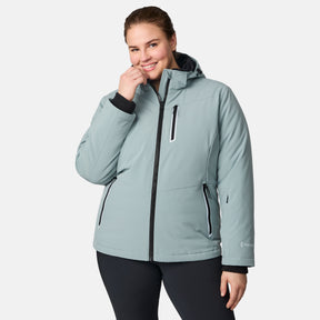 A woman smiles at the camera in a light blue Women's Plus Size FreeCycle® Thermo Super Softshell® II Jacket by Free Country, featuring black accents, zippered pockets, a high collar, and water-resistant fabric. She stands against a plain white background.