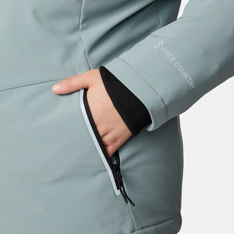 A woman wears the Free Country Women's Plus Size FreeCycle® Thermo Super Softshell® II Jacket in light gray, placing her hand into a zippered pocket; only her lower arm and hand are visible.