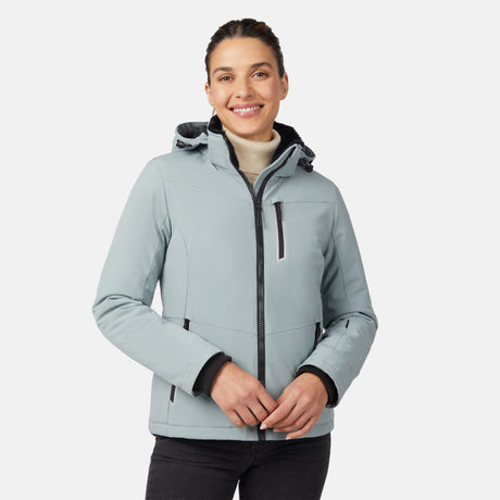 A woman smiles while wearing the Free Country Women's FreeCycle® Thermo Super Softshell® II Jacket in light gray, featuring a hood, black zippers, and a high collar, standing against a plain white background.