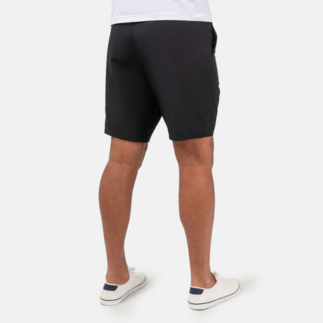 [Model is wearing a size Medium.] Man wearing Free Country Men's Tech Stretch Short II in Black, size M, made from moisture wicking stretch performance fabric featuring an elastic waistband with a drawcord and a side slant pockets, styled with a white t shirt #color_black