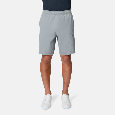 A person is shown from the waist down wearing Free Country Men's Tech Stretch Short II in light gray and white sneakers against a plain white background. The upper body is not visible.