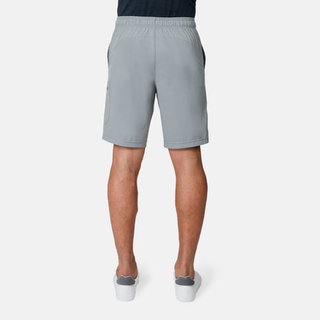 A person faces away, displaying the back view of the Free Country Men's Tech Stretch Short II in light gray with gray slip-on shoes. The moisture-wicking shorts are designed for comfort, set against a plain white background.