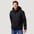 A man smiles while wearing a black Men’s Wild Land Mid Weight Jacket with zippered chest pockets and blue jeans.
