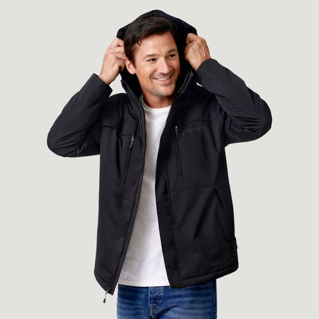 A smiling man wears a black Clearance Men’s Wild Land Mid Weight Jacket with zippered chest pockets over a white t-shirt and jeans.