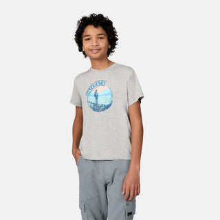 A smiling child with curly hair wears the Free Country Boys' Microtech® Graphic Crew Neck Shirt in light gray, featuring an “Explorer” graphic, paired with light gray cargo pants, standing against a plain white background.
