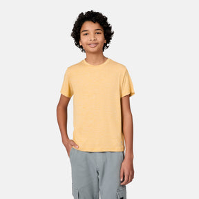 A smiling boy with curly hair wears a yellow Free Country Boys' Microtech® Crew Neck Shirt and light gray cargo shorts, standing with one hand in his pocket against a plain light background.