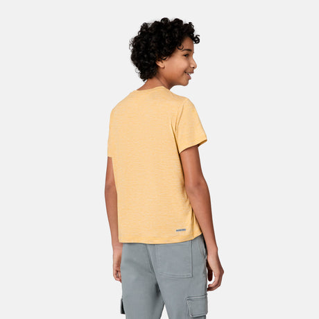 A young person with curly hair, wearing a yellow Free Country Boys' Microtech® Crew Neck Shirt and gray cargo pants, stands facing away from the camera and smiles over their shoulder against a plain light background.