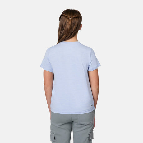 A girl with long brown braided hair stands facing away, wearing a light blue Free Country Girls' Microtech® Crew Neck Shirt and gray cargo pants against a plain white background.