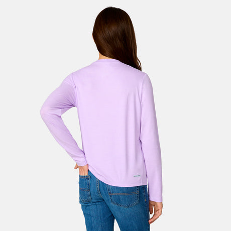 A girl with long brown hair, seen from behind, wears a Clearance Girls' Microtech® Long Sleeve Shirt in light purple and blue jeans, standing against a plain light gray background with one hand on her hip.