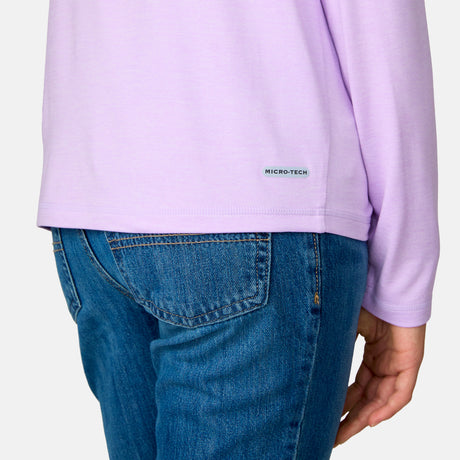 A person wearing blue jeans and a Girls' Microtech® Long Sleeve Shirt by Clearance, in light purple, featuring a small Micro-Tech label near the hem, is shown from the waist down with one arm relaxed at their side.