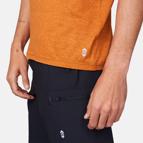 Close-up of a person wearing an orange Men’s Super Soft Microtech® Short Sleeve Crew Tee and black pants, both featuring a small white chevron logo.