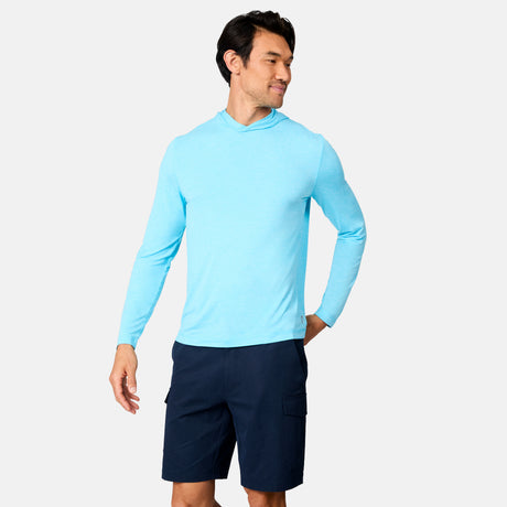 A man models the Free Country Men's Microtech® Hooded Graphic Sunshirt in light blue and dark navy cargo shorts against a plain white background, looking left with a slight smile.