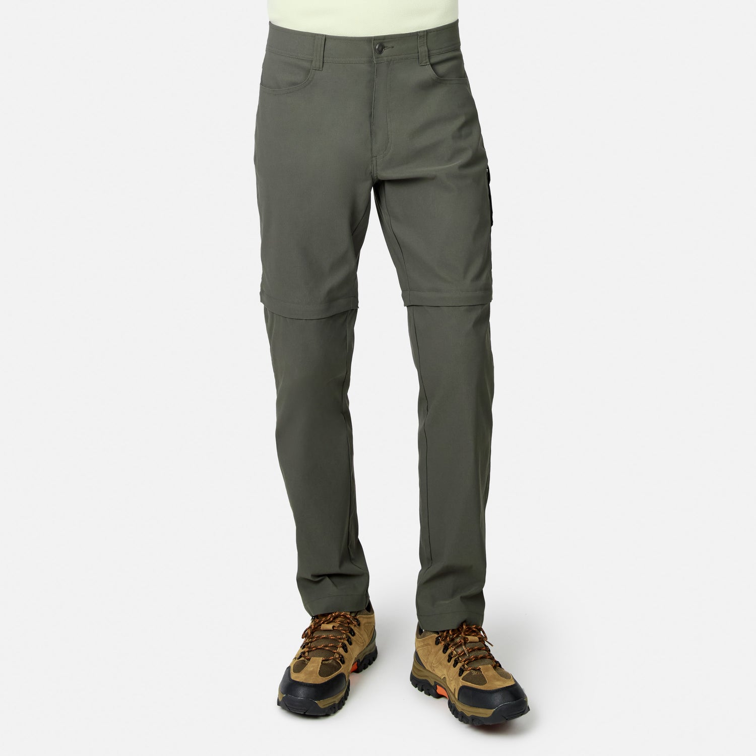 Lower body visible: person wears Free Country Men’s Nylon Stretch Convertible Pant in olive green—four-way stretch, water-repellent, converts to shorts via below-knee zippers—paired with brown hiking boots. Plain white background.