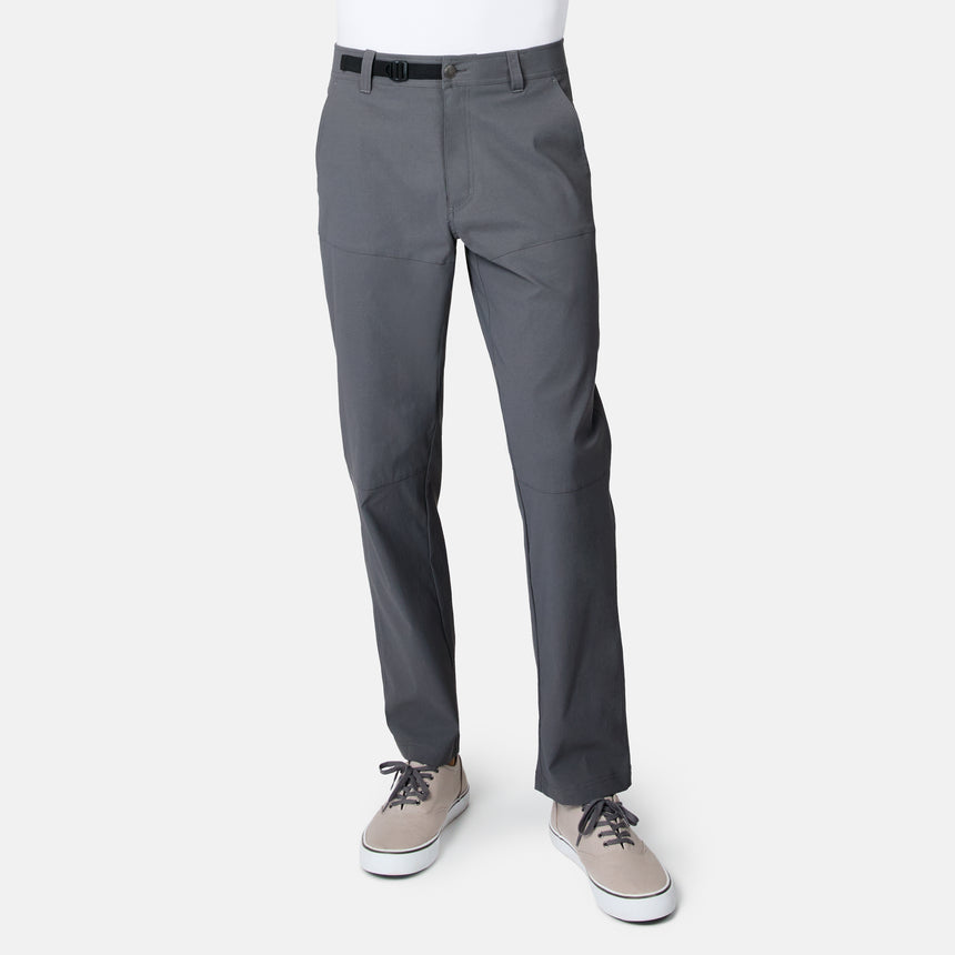 A man wears Free Country’s Men’s Nylon Stretch Casual Trek Pant in Coal, paired with a black belt and beige lace-up shoes, standing against a plain white background.