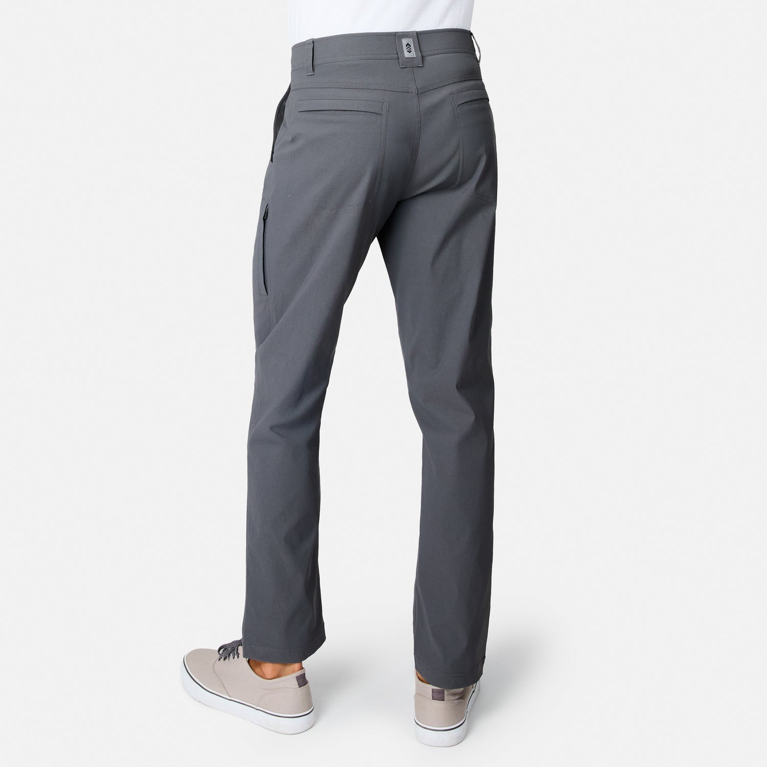 Person wearing Free Country Men’s Nylon Stretch Casual Trek Pant in gray with light gray sneakers, shown from the back on a white background. These comfort stretch pants feature multiple pockets, including a zippered pocket on the right leg.