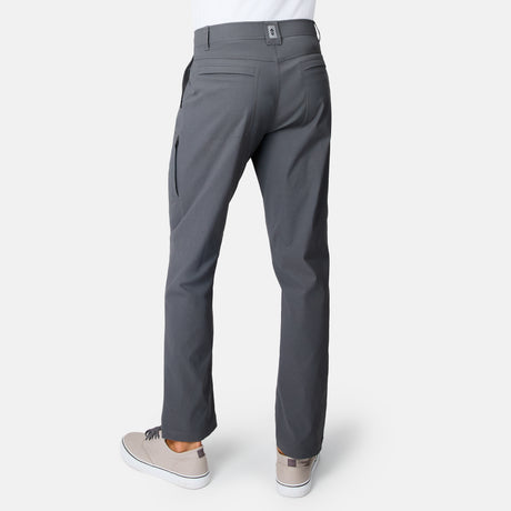 Person wearing Free Country Men’s Nylon Stretch Casual Trek Pant in gray with light gray sneakers, shown from the back on a white background. These comfort stretch pants feature multiple pockets, including a zippered pocket on the right leg.