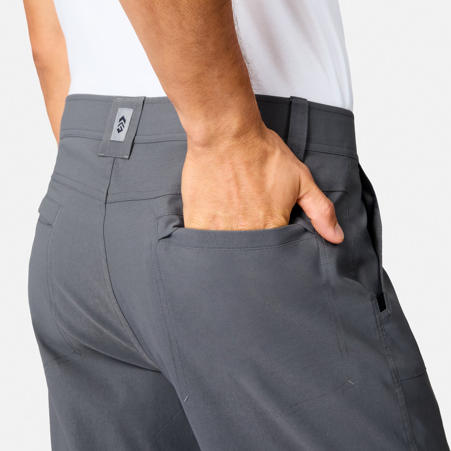 A person wearing Free Country Men’s Nylon Stretch Casual Trek Pant in gray and a white shirt is shown from the back, with their right hand partially inside the back pocket.