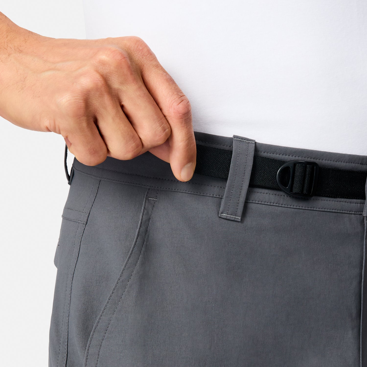 A person adjusts the black waistband of Free Country Men’s Nylon Stretch Casual Trek Pant in gray, featuring a built-in belt. They’re paired with a white shirt for a sleek, versatile look.
